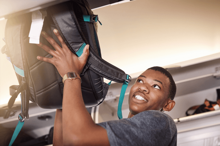 a man puts his backpack in overhead storage on a plane